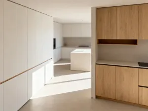 Przytulny mały salon z beżową sofą, drewnianym stolikiem i jasnymi ścianami, utrzymany w minimalistycznym stylu.